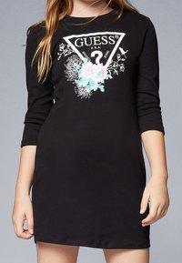 Musta puuvillamekko, jossa on kolme neljänneksen pituista hihaa. Mekossa on valkoinen kolmion muotoinen logo sekä vaaleansinisiä ja vaaleanpunaisia kukka-aiheisia koristeita. Mekon pinta on sileä.