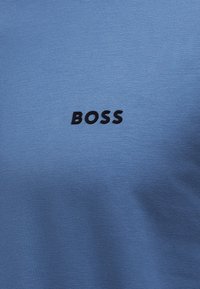 Μπλε ύφασμα με τη λέξη «BOSS» τυπωμένη με μαύρα, κεντραρισμένη στο υλικό.