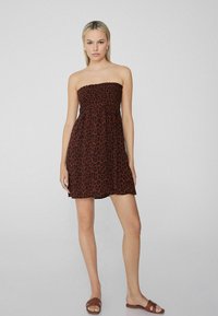 Robe brune sans bretelles avec un motif léopard, en tissu léger, et un bodice ajusté s'évasant en jupe évasée. Design simple.