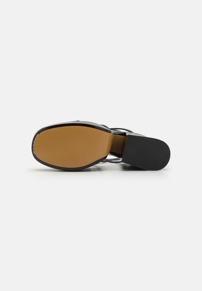 Sandal negru cu breteaua la gleznă, având un superior neted, o siluetă elegantă, o branț de nuanță bej și un toc solid negru; talpa de cauciuc pentru aderență.