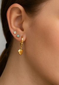 Goldene, herzförmige, hängende Ohrringe mit einer strukturierten Oberfläche, kombiniert mit einem Steckerohrring mit einem klaren Stein und einem türkisfarbenen Akzent.