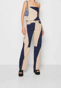 Top corto a patchwork beige e blu navy e pantaloni a gamba larga, in cotone, con motivi geometrici. Scarpe nere chunky con platform.