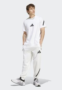 Hvit treningstrøye med svart Adidas-logo og detaljer. Kombinert med hvite joggebukser med svarte striper og svarte treningssko.
