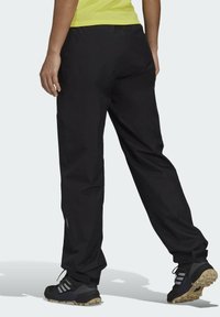 Pantaloni sportivi neri realizzati in materiale leggero con vita elasticizzata, vestibilità tapered e cinture regolabili alla caviglia. Abbinati a scarpe nere.
