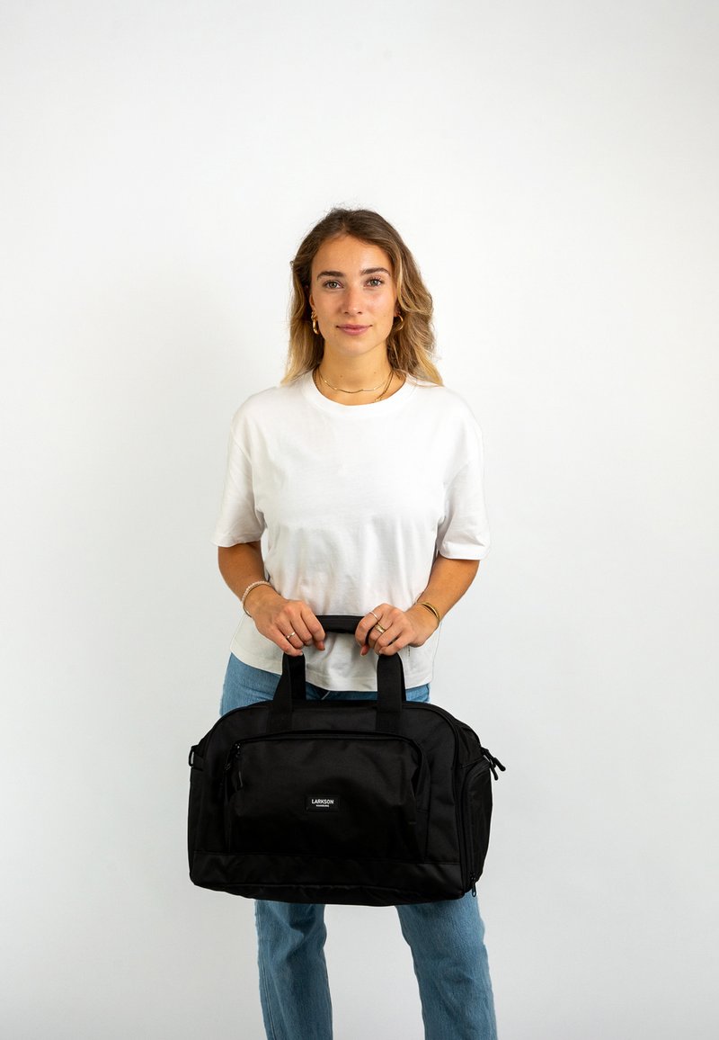 Fekete sporttáska tartós anyagból, két tetején lévő fogantyúval, elülső cipzáras zsebbel és logós részletekkel. Strukturált kialakítás, tágas belső térrel.