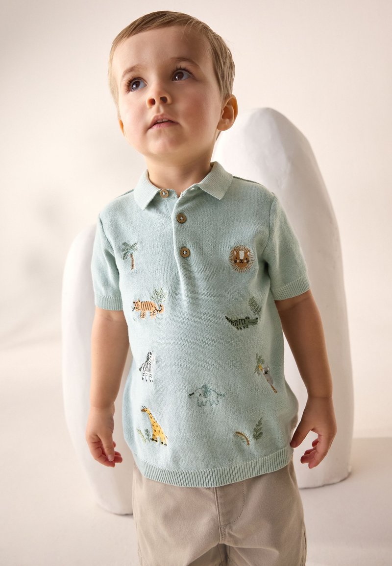 Polo de punto azul claro con mangas cortas, con bordado de animales coloridos, botones en el cuello y dobladillo acanalado.