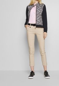 Czarna i biała kurtka w panterkę z jednolitymi czarnymi rękawami, jasnoróżowa bluzka, beżowe krótkie spodnie i czarne trampki ze złotymi akcentami.