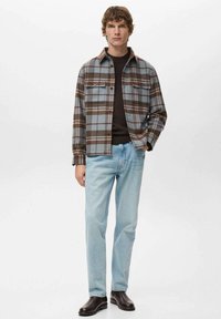 Camisa de franela a cuadros en azul y marrón, con botones en el frente y dos bolsillos en el pecho. Combinada con vaqueros azul claro y zapatos oscuros. Diseño sencillo y casual.