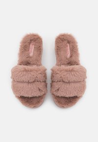 Une paire de chaussons ouverts en peluche rose avec des doubles lanières épaisses, un intérieur doux et une étiquette de marque visible sur un fond blanc.