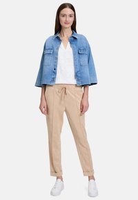 Giacca di jeans con due tasche anteriori; top bianco con motivo testurizzato; pantaloni beige con coulisse; sneakers bianche.