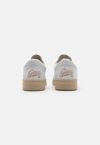 Vita sneakers med en beige sula, mjuka mockadetaljer och broderad "Gant"-logotyp på hälen. Klassisk snörningsdesign.