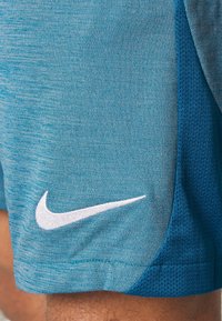 Shorts deportivos azules con el logo del swoosh de Nike en blanco, llevados en el muslo de una persona, mostrando paneles de tela texturizada y de malla.