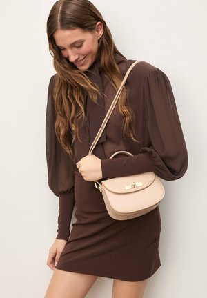 Svetlo bež ročna torbica z zaobljeno obliko in minimalnim zlatim okovjem. Material je videti gladek, dopolnjuje pa ga usklajen pašček.