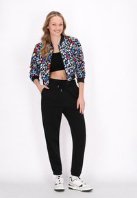 Giacca bomber nera con stampa leopardata multicolore, top corto nero e pantaloni jogger neri. Sneakers bianche con accenti neri.