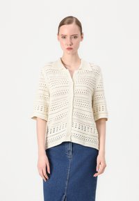 Strikket kortermet cardigan i kremfarge med knappelukking foran, som har et strukturert åpent maskemønster og flat krage.