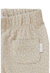 Pantalon vert clair avec une taille douce et élastique, arborant un motif à pois en rose pâle, et une poche au dos avec une étiquette de marque.