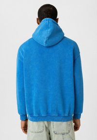 Blauwe hoodie van zacht materiaal, met een trekkoordcapuchon, lange mouwen en ribbelboorden aan de mouwen en onderkant. De achterkant heeft een glad, naadloos ontwerp.