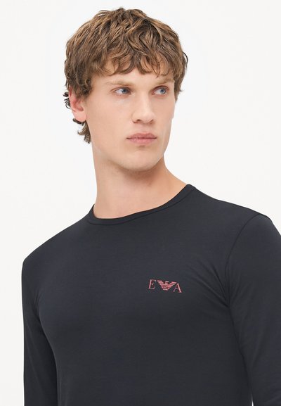 Chemise noire à manches longues en matière douce, avec un petit logo rouge sur la poitrine, un col rond et une silhouette ajustée.