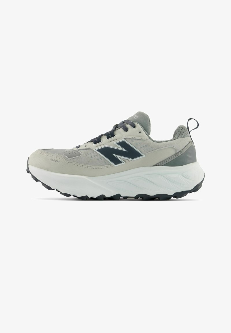 Baskets de sport gris clair et blanc avec des lacets noirs, une semelle noire, une plateforme rembourrée et un logo sombre sur le côté.