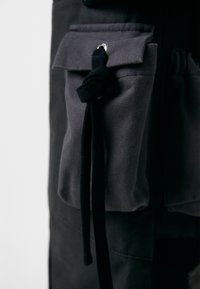 Grijze stoffen utility pocket met een trekkoordsluiting, gemaakt van een houtachtige materiaalmix. Bevat een klep en metalen hardware voor bevestiging.