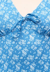 Μπλε φόρεμα με μικρά λευκά άνθη και λεπτομέρεια φιόγκου με κόμπο στη V-λαιμόκοψη σε υφασμένο ύφασμα.