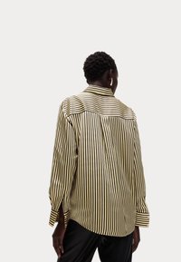 Camicia a righe gialla e nera, con colletto, maniche lunghe e spacchi laterali. Textura liscia con una vestibilità rilassata.
