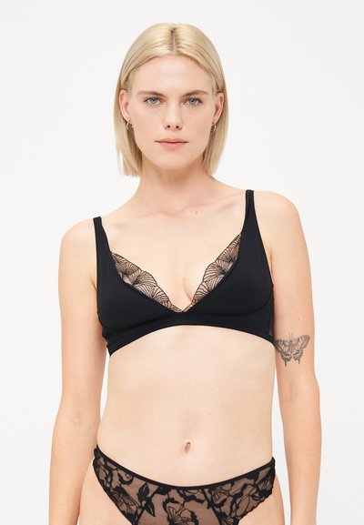 Sort trådløs bralette med en dyb V-udskæring med blonderkant, suppleret med matchende gennemsigtig sort undertøj med blomsterdesign.