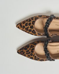 Leopardmuster-Spitzschuhe in Braun und Schwarz, mit einem schwarzen mit Edelsteinen besetzten Riemen über den Spann. Glatte Textur mit glänzender Oberfläche.