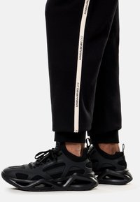 Zapatillas deportivas negras con materiales de malla y sintéticos, con suelas de goma curvas y cordones en blanco y negro contrastantes.