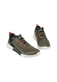 Athletic shoes in olive green and black, featuring mesh material, red accents, thick white sole, and textured detailing on the upper.