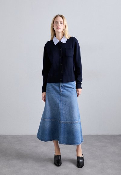 Cardigan in maglina blu navy con colletto e chiusura a bottoni sopra una gonna in denim azzurro chiaro. Le mule nere completano l'outfit.
