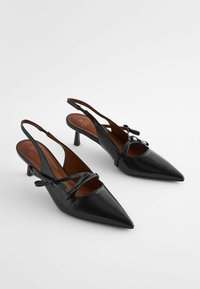 Black leather slingback heels with pointed toes, thin straps featuring bow accents, and a low block heel. Smooth texture and minimal design.