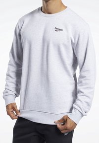 Szara bluza z okrągłym dekoltem, wykonana z miękkiego materiału, z małym czerwono-niebieskim logo Reebok na piersi oraz ściągaczami na mankietach i u dołu.