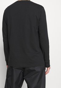 Svart långärmad t-shirt i bomull med rund halsringning och slät textur, visad bakifrån med minimal design.