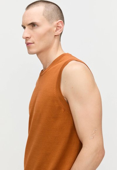 Haut sans manches dans une couleur rouille-orange, fabriqué en tissu doux, avec un col rond et des détails de couture soignés sur l'épaule.