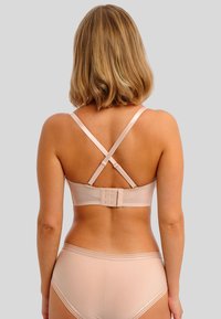 Nude bralette met een gladde afwerking, verstelbare kruislings verlopende banden en een haak-en-oogsluiting. Eenvoudig ontwerp met minimale details.