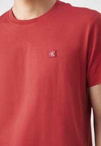Rød t-shirt med korte ærmer lavet af glat bomuld, med et lille broderet logo på venstre brystområde. Rund halsudskæring, minimalistisk design.
