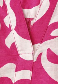 Tissu rose et blanc avec un grand motif floral abstrait et un col en V avec des coutures visibles.