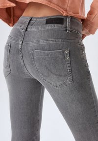 Jean skinny en denim gris avec une taille mi-haute, dotés de poches arrière et de détails de surpiqûres subtils. Étiquette en cuir sur la taille.