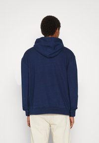 Dunkelblaues Kapuzensweatshirt mit lässiger Passform, strukturiertem Stoff, gerippten Bündchen und einer Kängurutasche an der Vorderseite. Minimalistisches Design.
