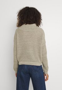 Vaaleanbeige neulottu neulepaita leveällä, käännetyllä kaula-aukolla ja pudotetuilla hartioilla, rento malli ja kuvioitu neulossilmukkakuvio.