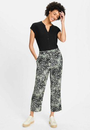 Black short-sleeve top with button closure, paired with wide-leg pants featuring a black and green abstract pattern, worn with light sneakers.