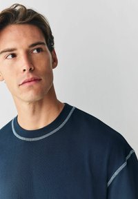 Granatowy sweter z okrągłym dekoltem i jasnoniebieskimi kontrastowymi szwami. Miękka faktura, krótkie rękawy, dopasowany wokół szyi.