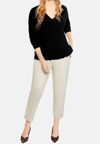 Pull noir en v, en tricot léger, associé à un pantalon crème à taille ajustée. Des escarpins léopard noir et marron complètent l'ensemble.