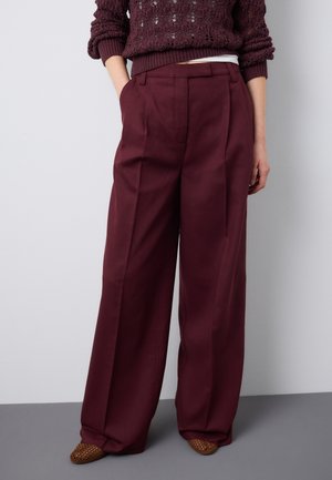 Mujer con pantalones anchos burdeos con pliegues delanteros, combinados con un suéter burdeos texturizado y zapatos marrones tejidos.