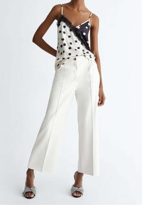 Un débardeur noir et blanc à pois avec des bordures en dentelle, associé à un pantalon large blanc taille haute. Des escarpins ouverts à motifs.