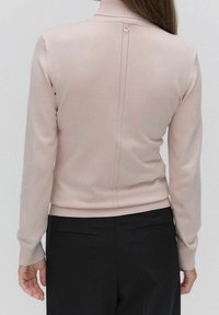 Maglione aderente rosa chiaro con colletto alto, con polsini e orlo a costine, caratterizzato da dettagli di cucitura visibili e un singolo accento circolare sul retro.