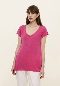 Tricou roz cu decolteu în V, cu mâneci scurte și volănașe, confecționat dintr-un material ușor, având o croială lejeră și detaliu de tiv cusut.