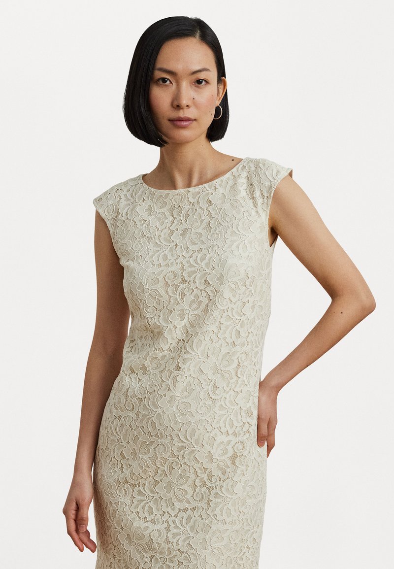 Creamo dressi með lace í fittum siluett, skautahendur, blómamynstur, og mjúkan áferð, borið af fyrirsætunni gegn hvítri bakgrunni.