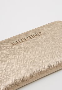 Gold textured pouch with embossed "VALENTINO" logo. Smooth surface, rectangular shape, and a subtle pattern of raised dots.